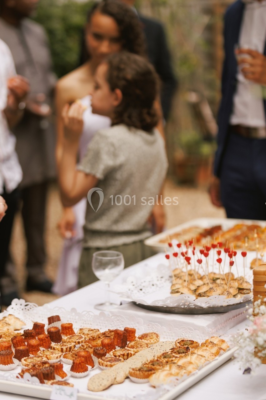 Plateau de pâtisseries et amuse-bouches sur une table lors d'un événement en extérieur avec des convives en arrière-plan.