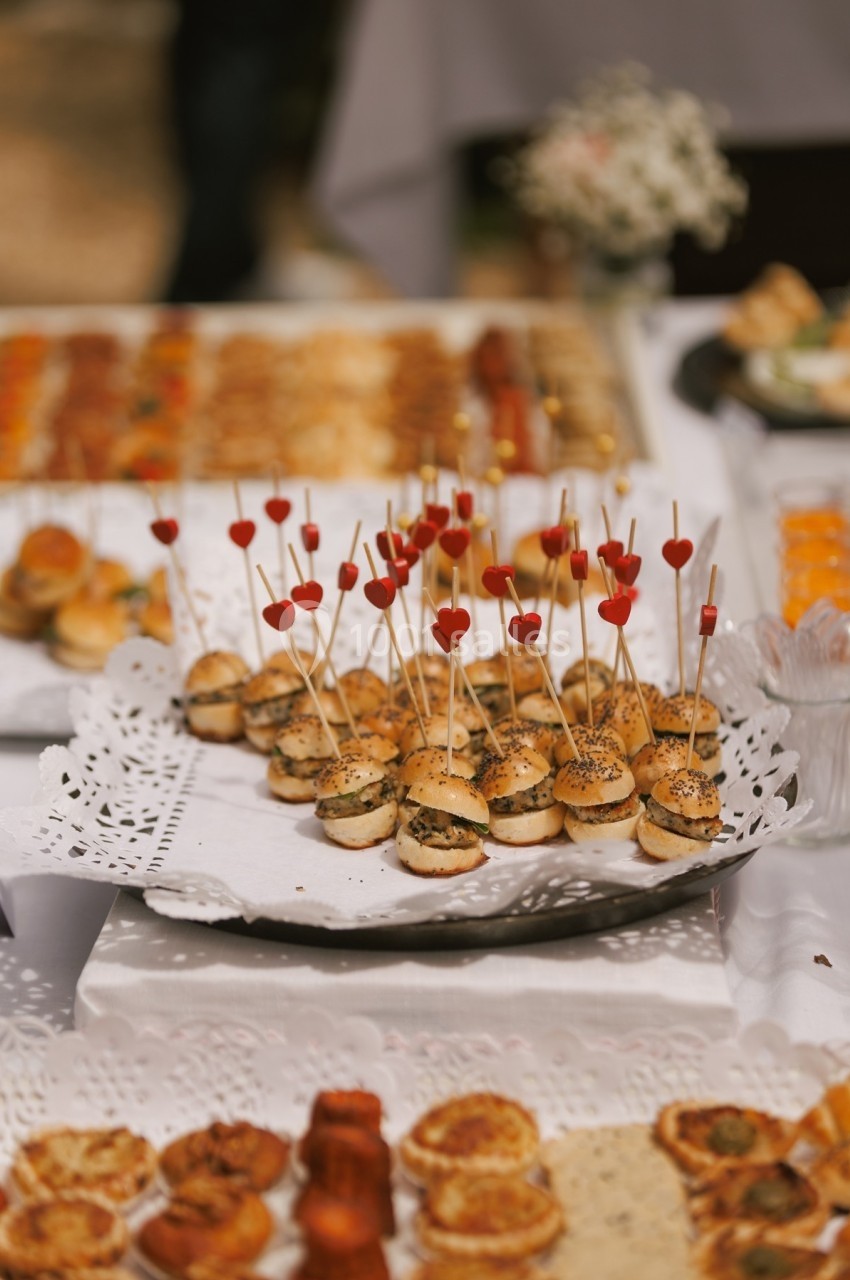 Plateau de mini-burgers garnis, décorés de piques rouges en forme de cœur, sur une table de buffet.