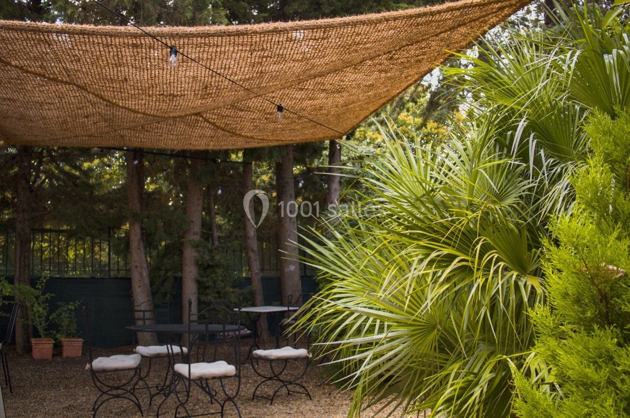 Terrasse extérieure ombragée avec des tables et des chaises, entourée de végétation dense et d'arbres.
