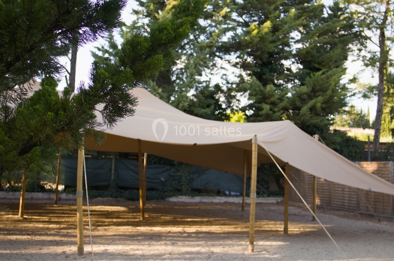 Toile tendue beige montée sur des poteaux en bois, installée dans un espace extérieur entouré d'arbres.