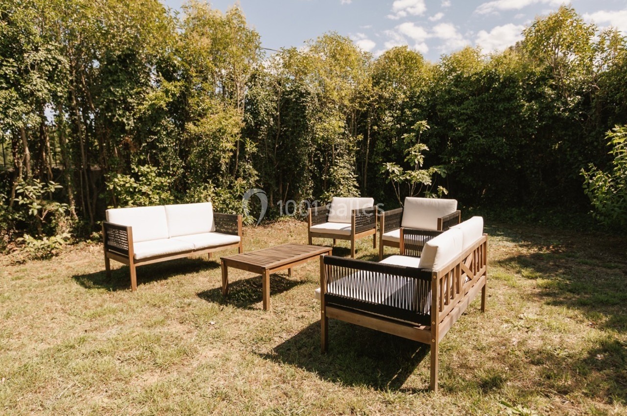 Salon de jardin en bois avec coussins blancs, composé de fauteuils, d'un canapé et d'une table basse, sur une pelouse.