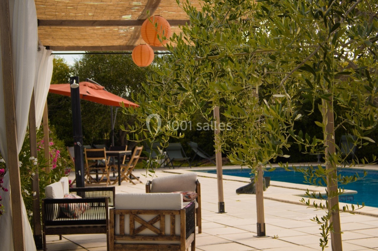 Terrasse avec mobilier en bois, piscine, parasol orange et pergola ombragée entourée de végétation.