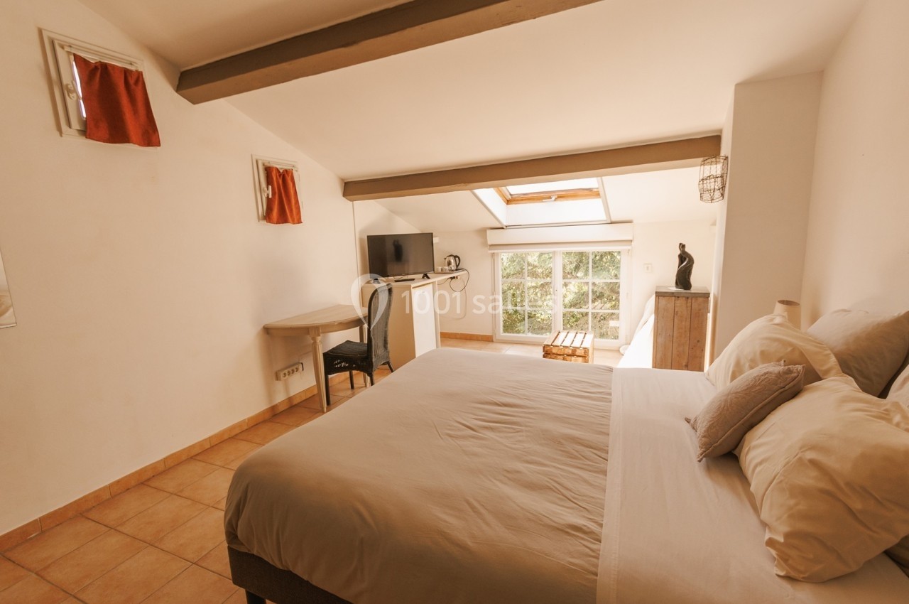 Chambre lumineuse avec lit double, bureau, télévision et fenêtre de toit laissant entrer la lumière naturelle.
