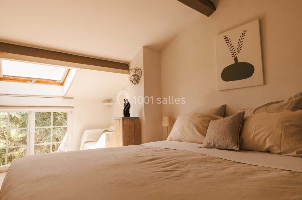 Chambre lumineuse avec lit double, fenêtre de toit, tableau décoratif et mobilier en bois clair.