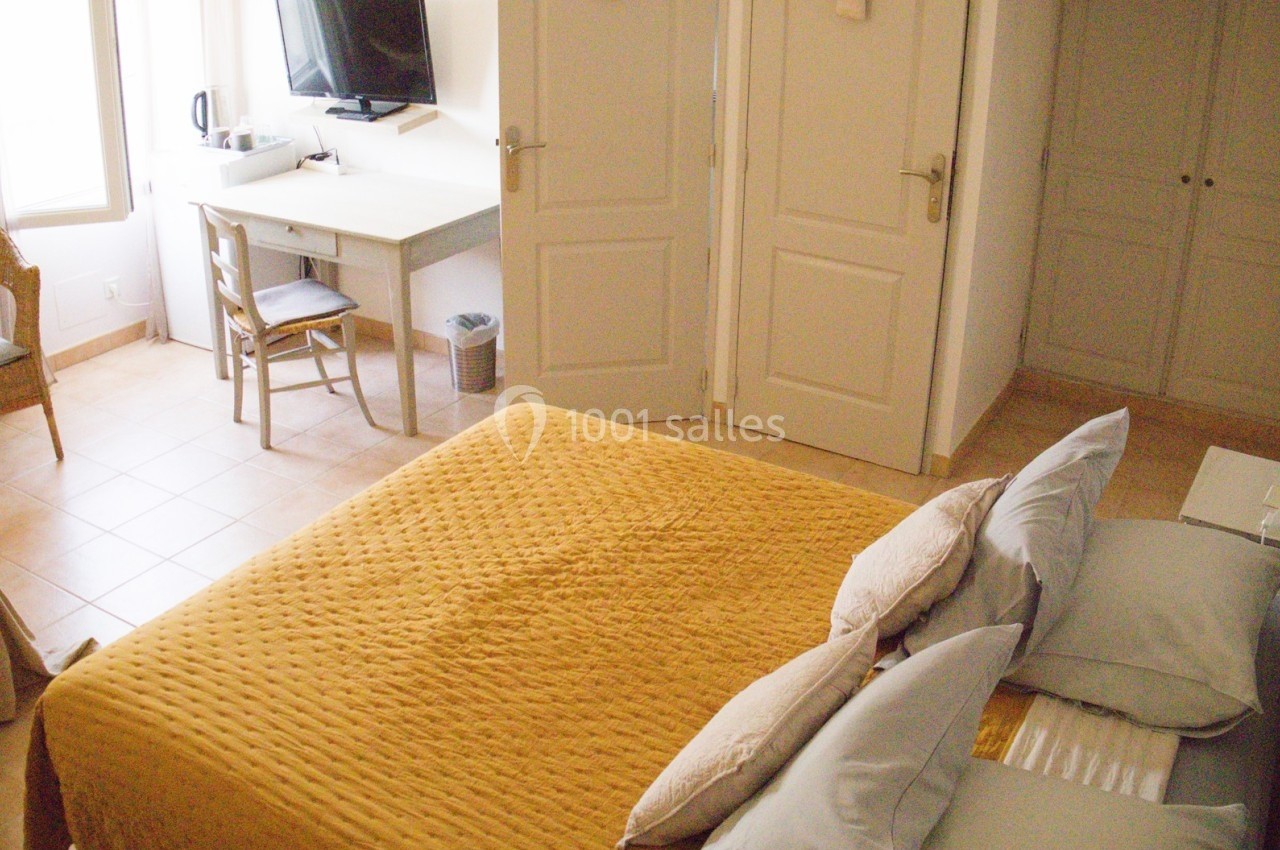 Chambre lumineuse avec lit double, bureau, chaise, télévision murale et mobilier en bois clair.