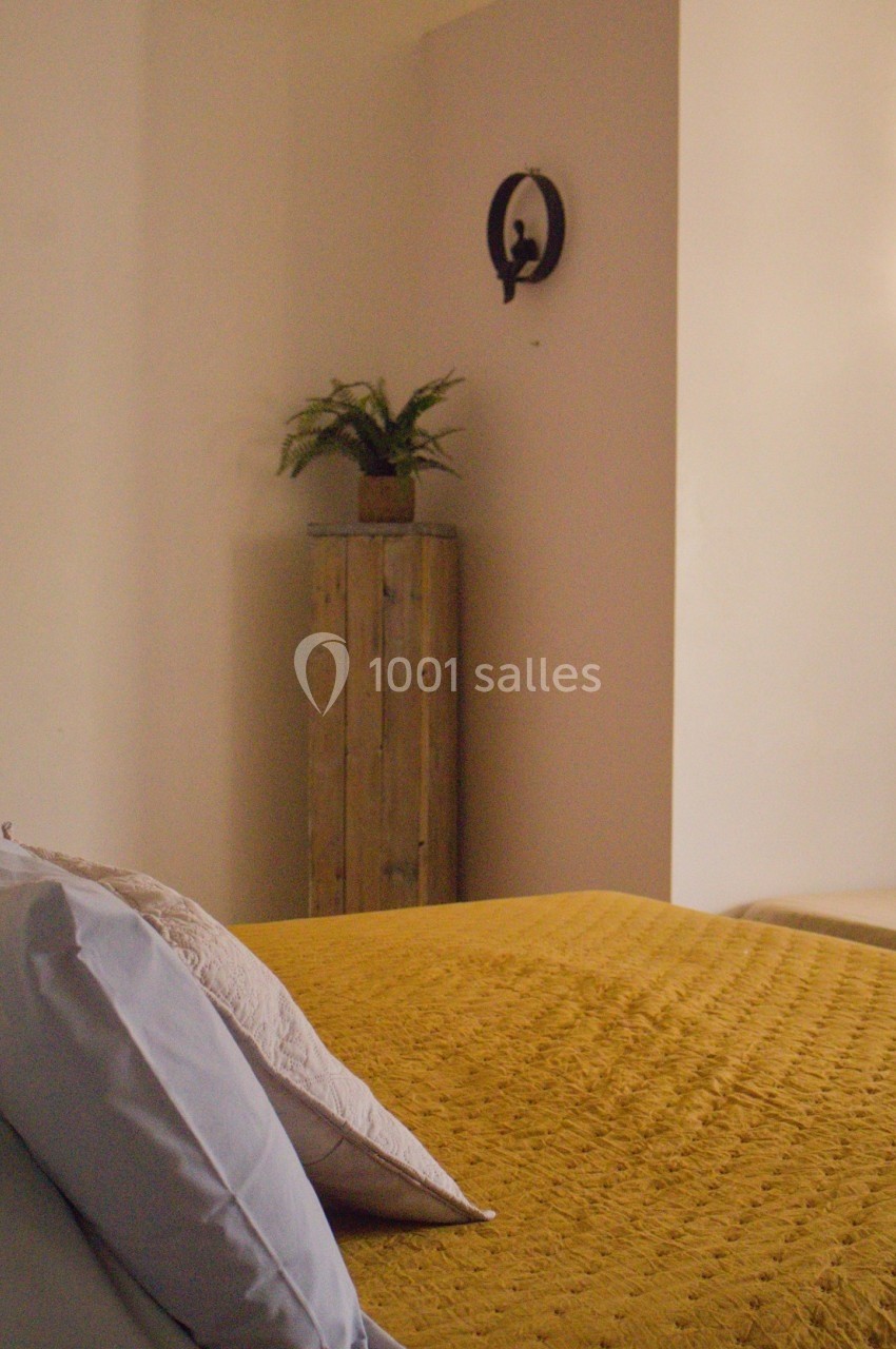 Lit avec couvre-lit jaune et oreillers, plante sur un meuble en bois et décoration murale dans une pièce lumineuse.
