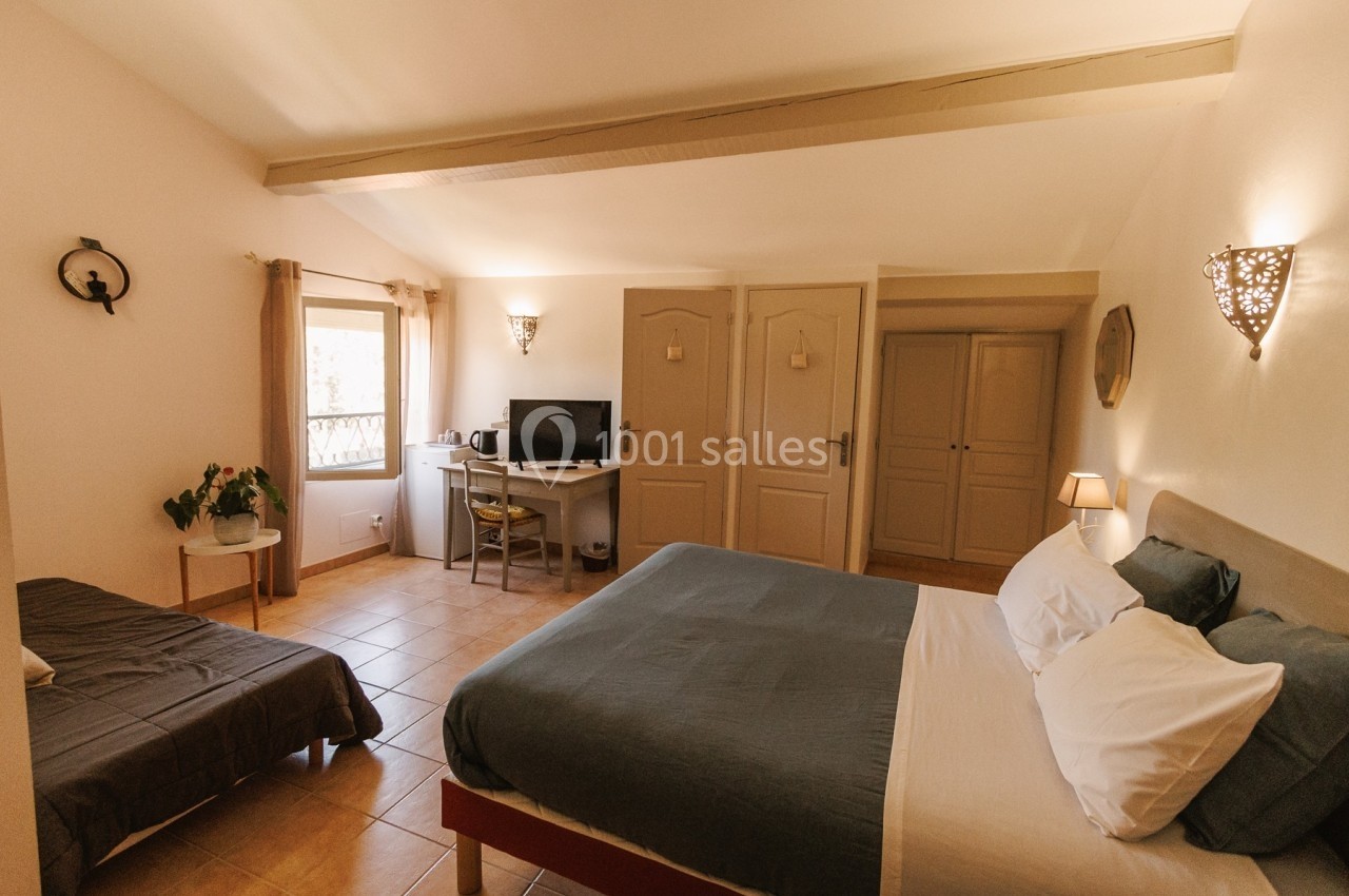 Chambre lumineuse avec lit double, lit simple, bureau avec écran, armoire et fenêtre laissant entrer la lumière naturelle.
