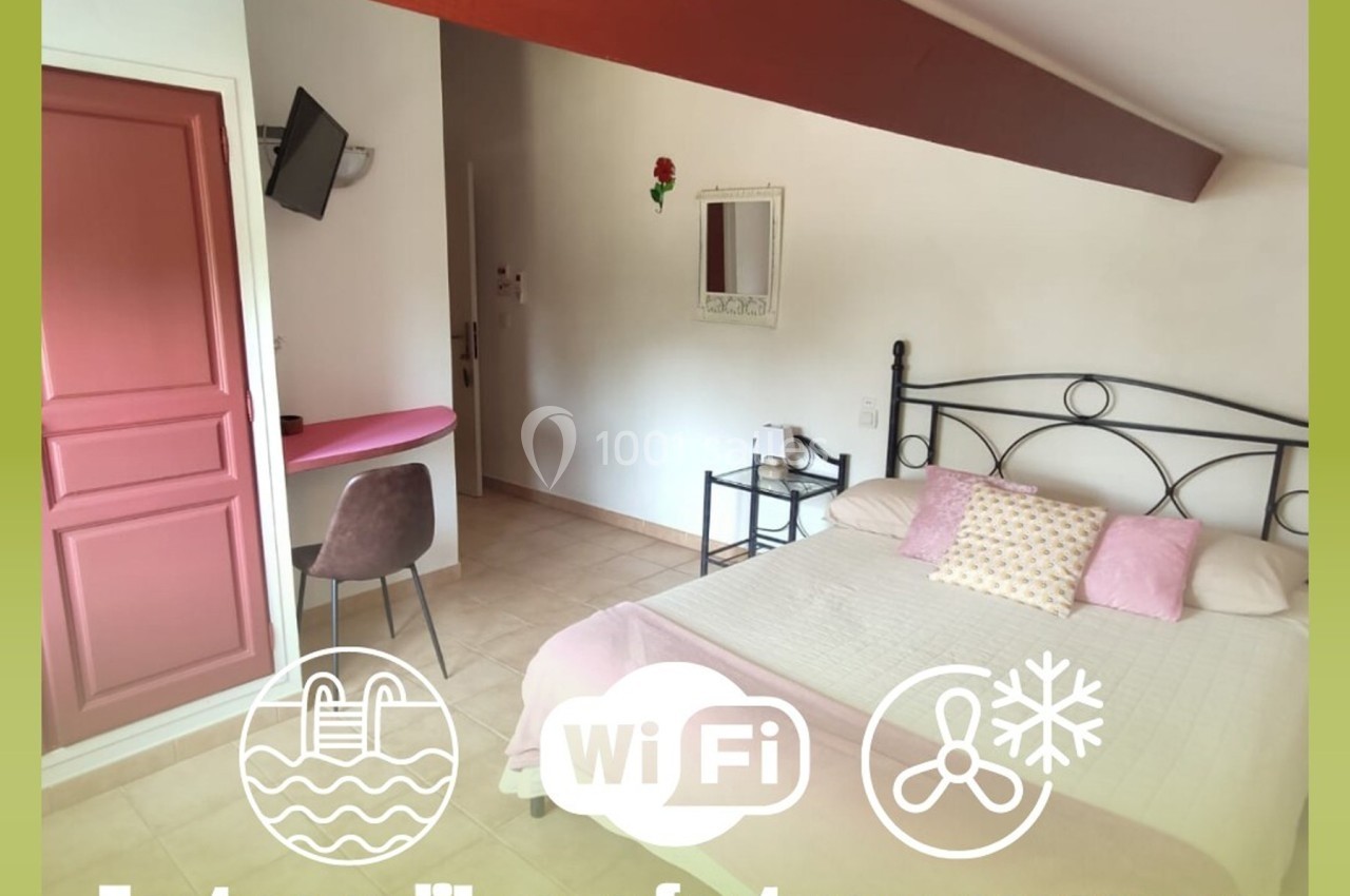 Chambre lumineuse avec lit double, bureau, télévision murale et décoration simple dans un cadre accueillant.
