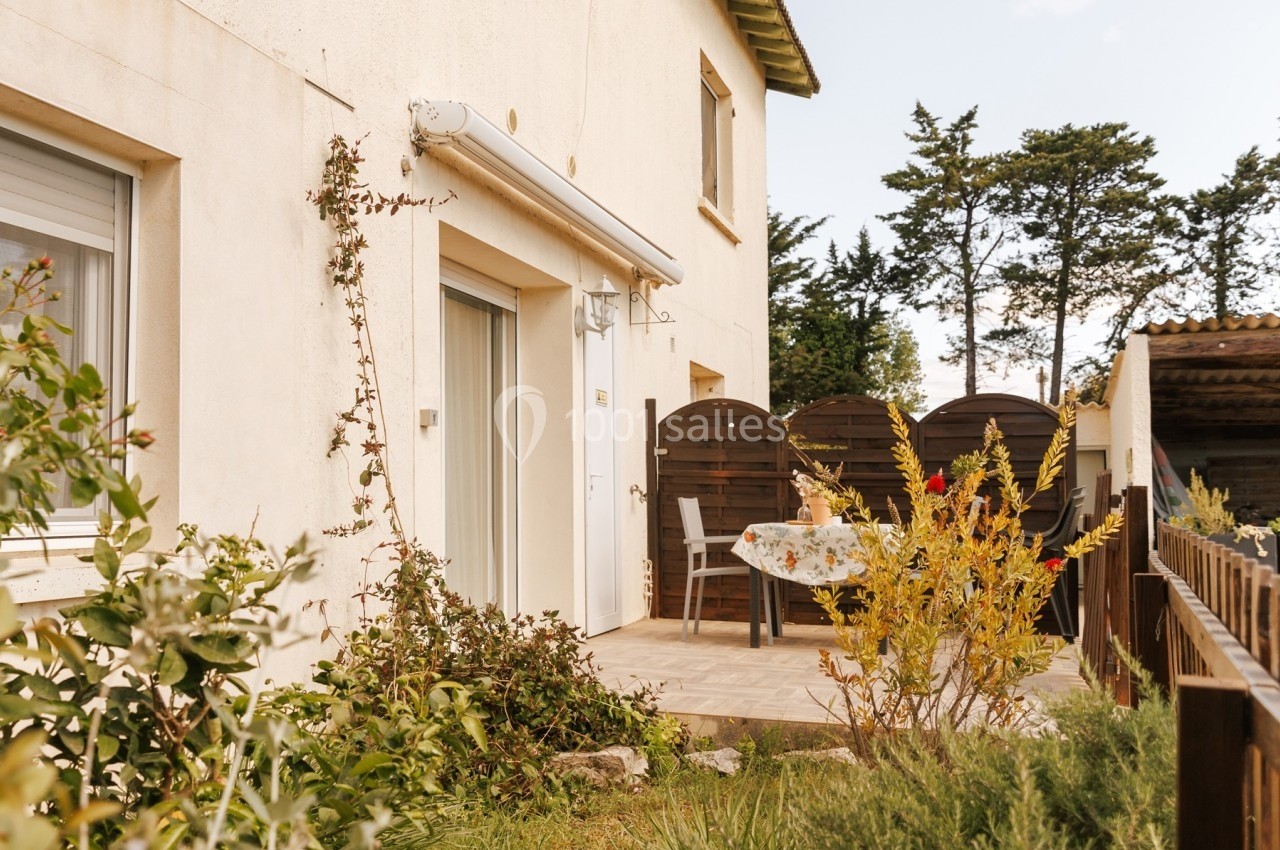 Terrasse extérieure d'une maison avec table, chaises et végétation environnante sous un ciel dégagé.