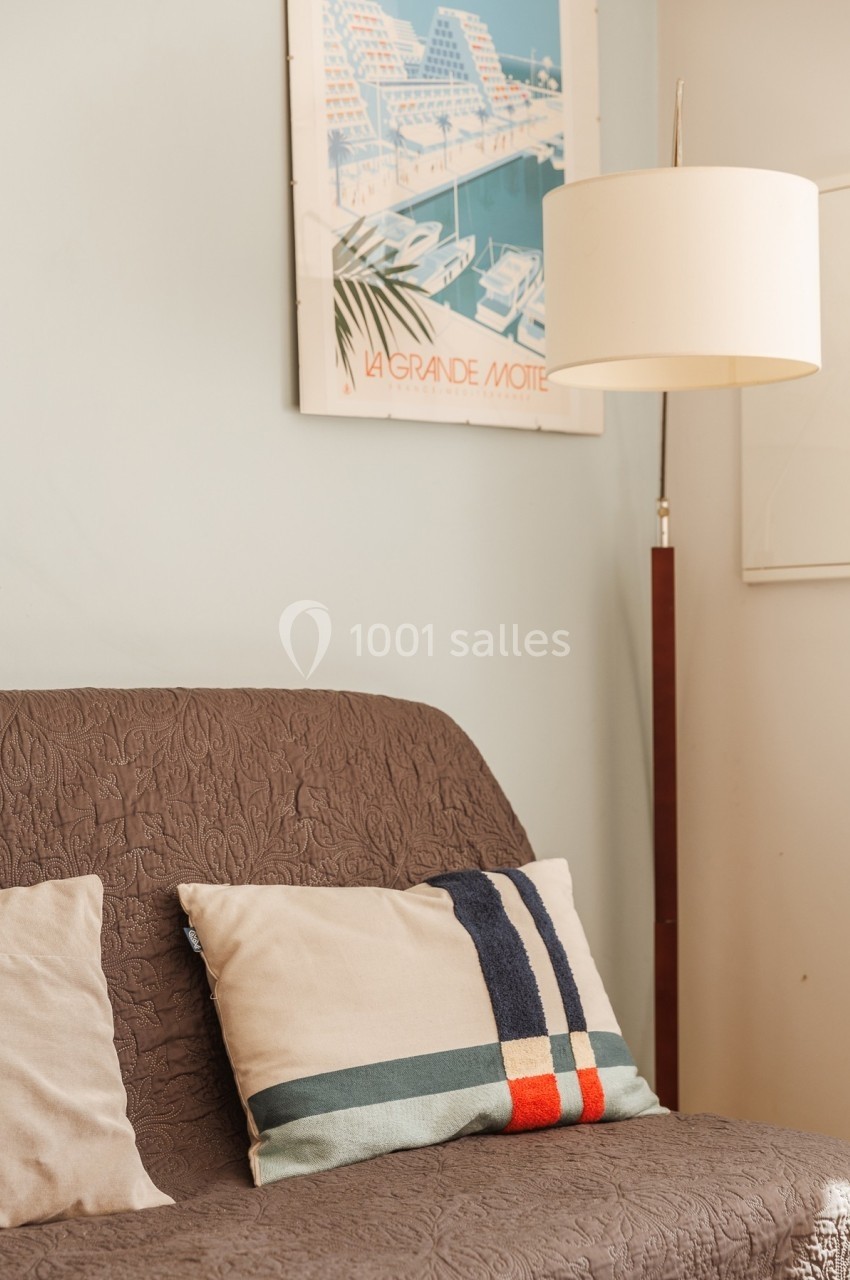 Canapé brun avec coussins décoratifs, lampe sur pied et affiche rétro en arrière-plan dans un intérieur lumineux.
