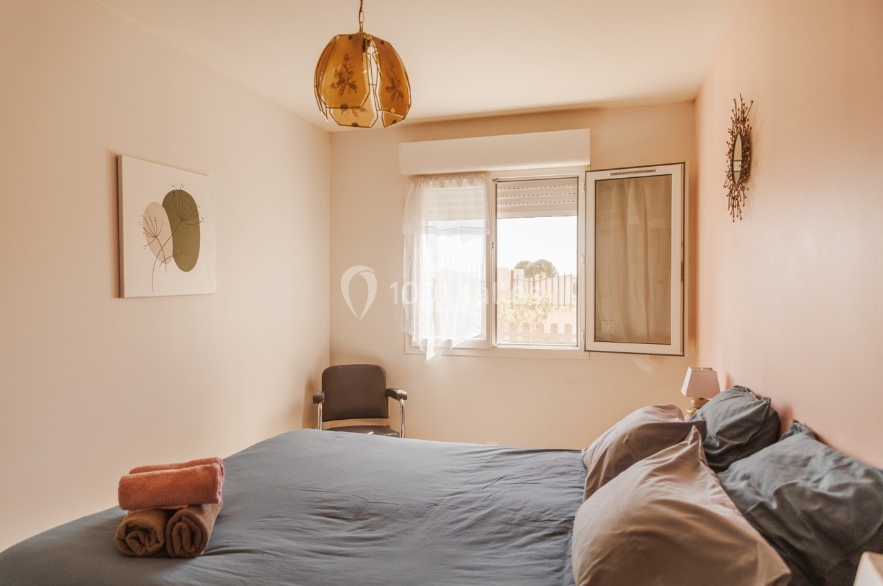 Chambre lumineuse avec lit double, linge plié, fenêtre ouverte et décoration murale minimaliste.