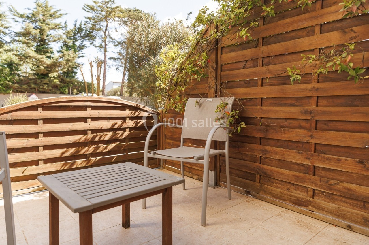 Petite terrasse avec table et chaise en métal, entourée de panneaux en bois et de plantes grimpantes.