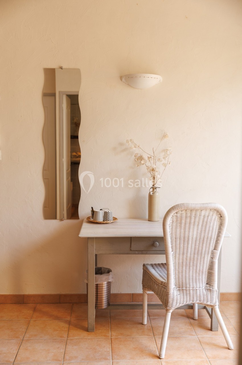Bureau en bois clair avec chaise en rotin, miroir ondulé, vase avec fleurs séchées et lumière naturelle.