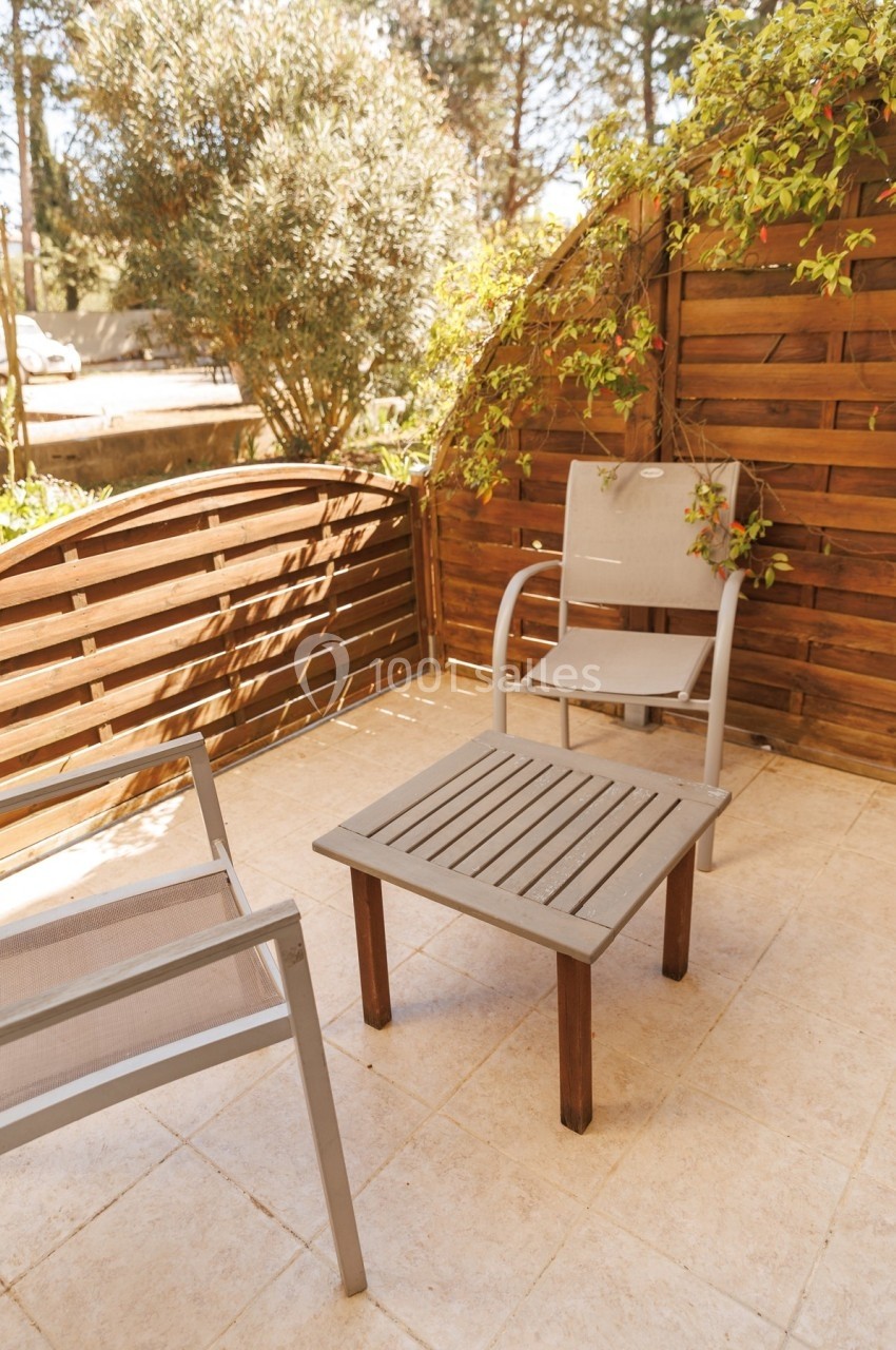 Deux chaises et une table en bois sur une terrasse carrelée entourée de panneaux en bois et de végétation.