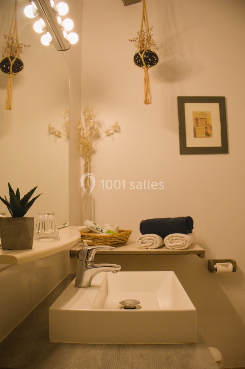 Lavabo moderne avec miroir, serviettes pliées, plantes décoratives et éclairage chaleureux dans une salle de bain.
