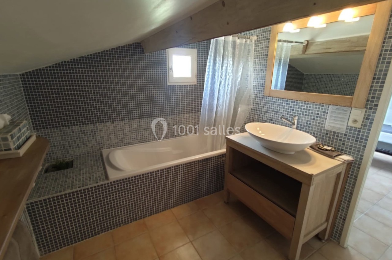 Salle de bain mansardée avec baignoire, vasque sur meuble en bois, carrelage mosaïque bleu et lumière naturelle.