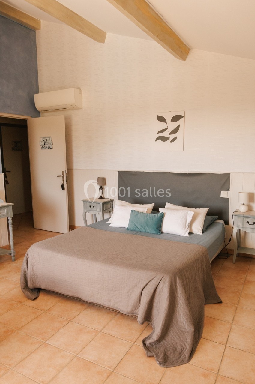 Chambre lumineuse avec lit double, coussins décoratifs, tables de chevet et murs clairs.