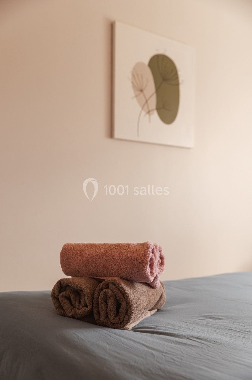 Serviettes pliées sur un lit dans une pièce au décor minimaliste avec un tableau abstrait au mur.