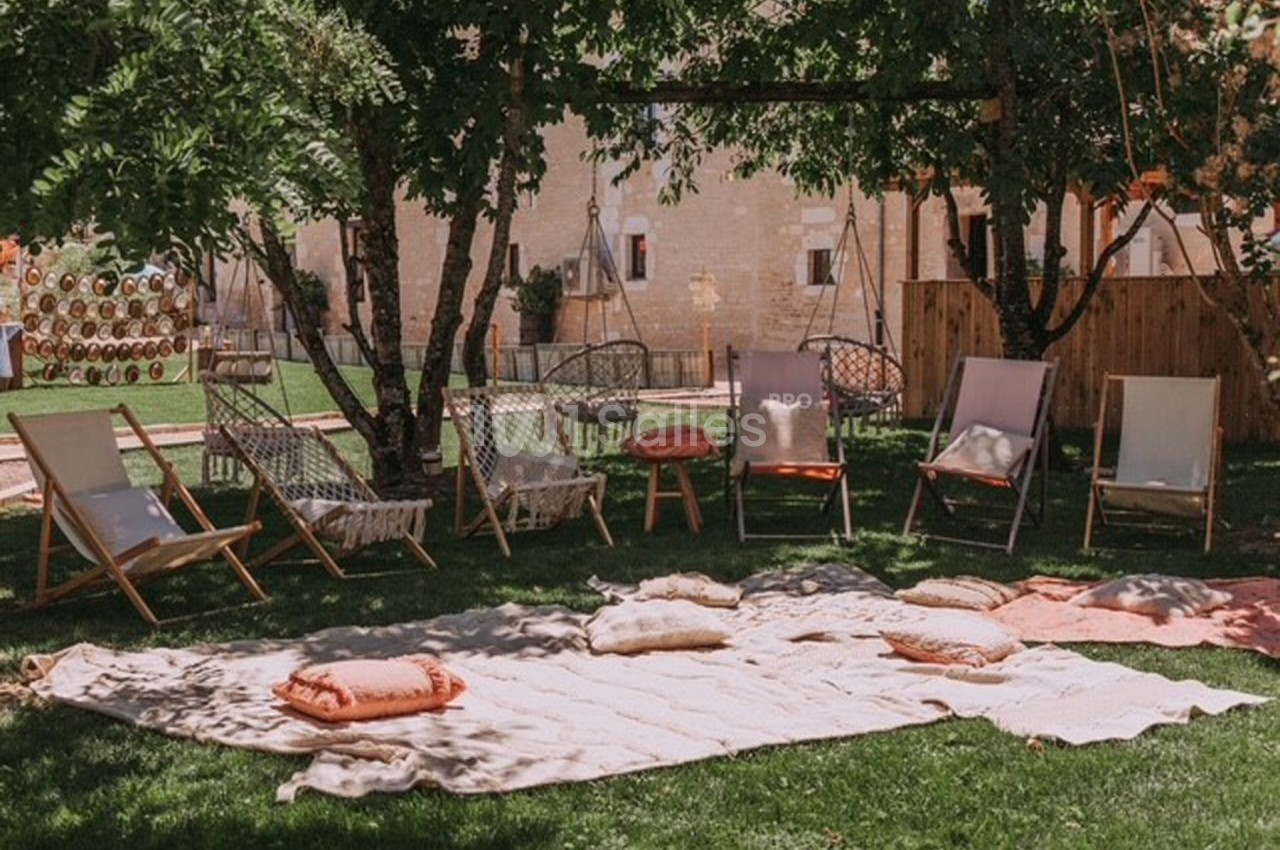 Chaises longues et coussins disposés sur une pelouse ombragée, entourés d'arbres et d'une ambiance extérieure paisible.