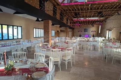Salle de réception décorée avec des guirlandes colorées, tables rondes dressées et chaises blanches.