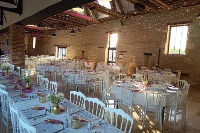 Salle de réception décorée avec des guirlandes colorées, tables rondes dressées et chaises blanches.