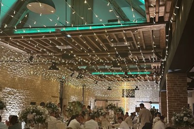 Salle de réception décorée avec des guirlandes colorées, tables rondes dressées et chaises blanches.