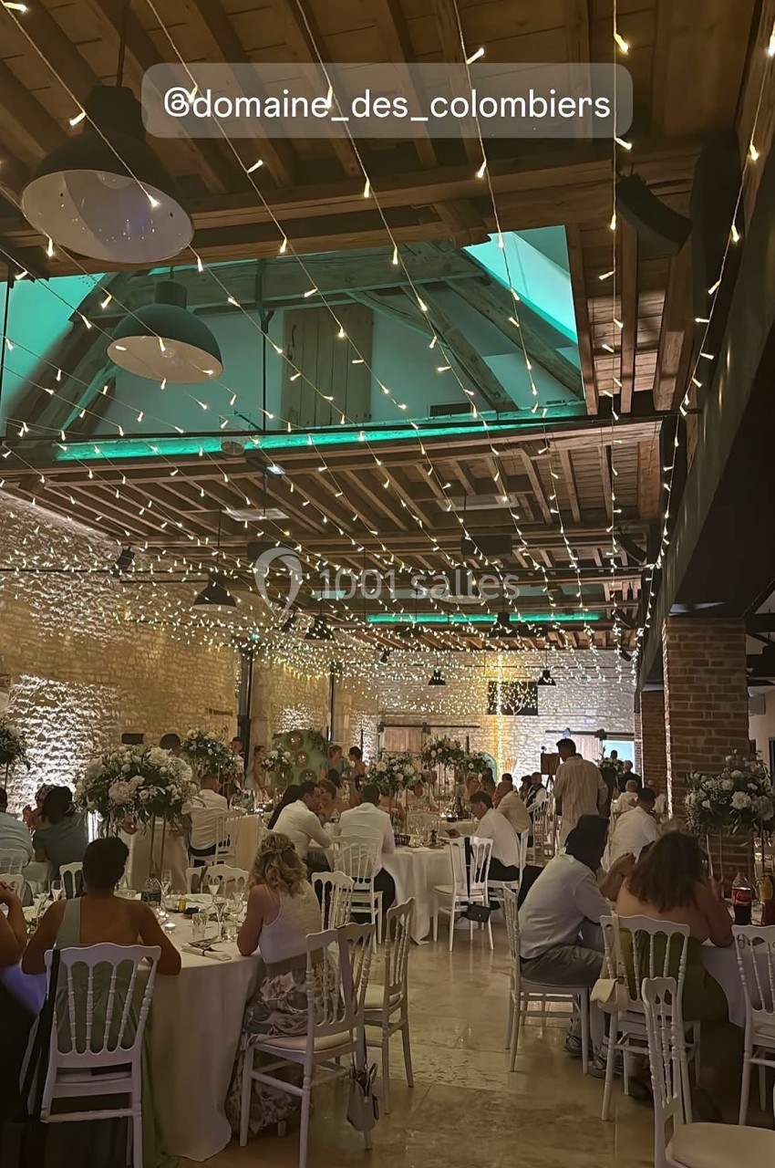 Salle de réception décorée de guirlandes lumineuses, avec des invités assis à des tables élégamment dressées.