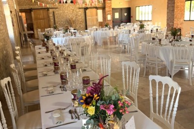 Salle de réception décorée avec des guirlandes colorées, tables rondes dressées et chaises blanches.
