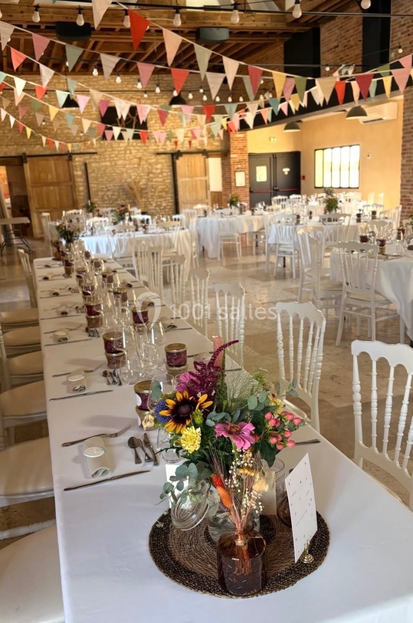 Salle de réception décorée avec des guirlandes de fanions, tables dressées et centres de table fleuris.