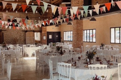 Salle de réception décorée avec des guirlandes colorées, tables rondes dressées et chaises blanches.