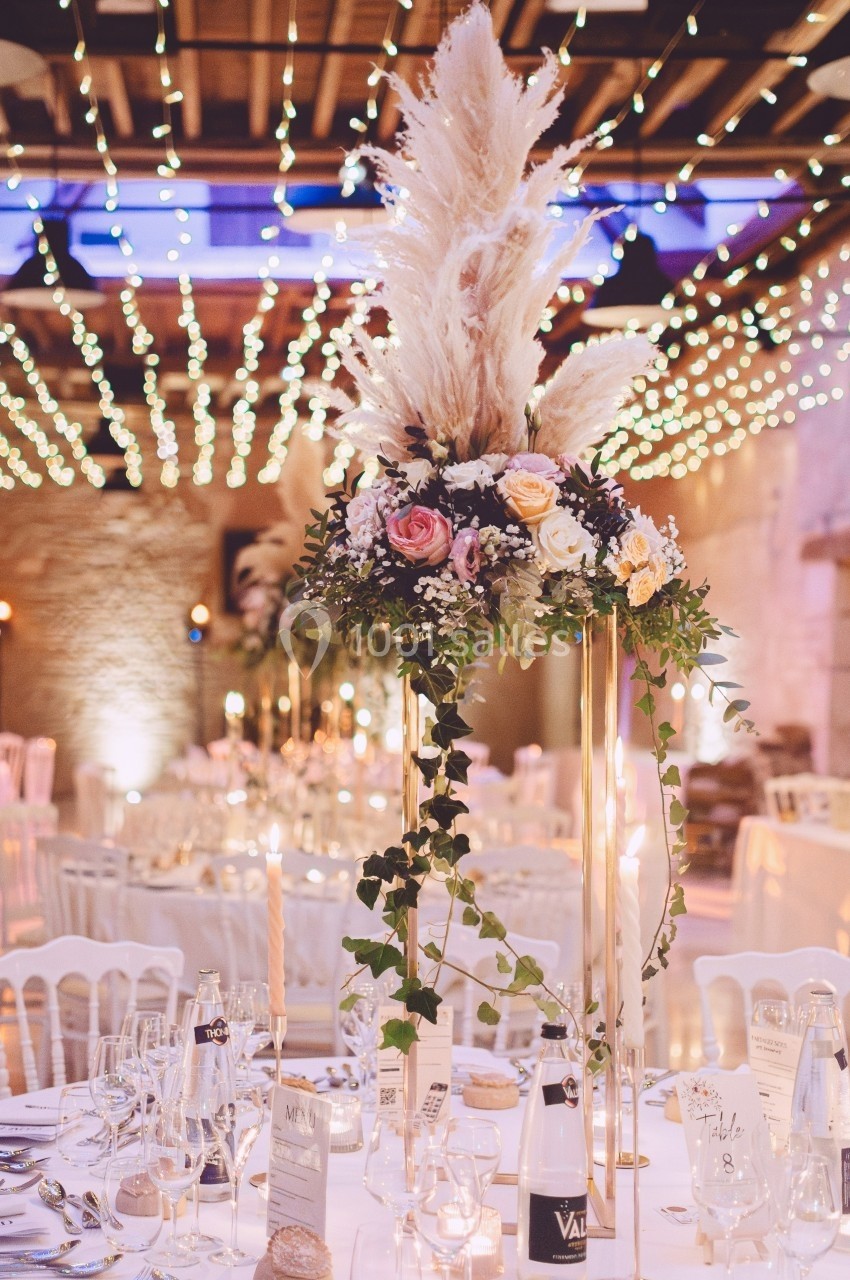 Centre de table floral avec pampas, roses et feuillage, sous un plafond décoré de guirlandes lumineuses.