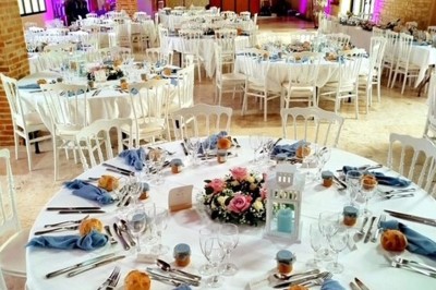 Table en bois avec un chapeau, un flacon de parfum, des sandales, un bouquet de fleurs et une bague devant un mur de briques.