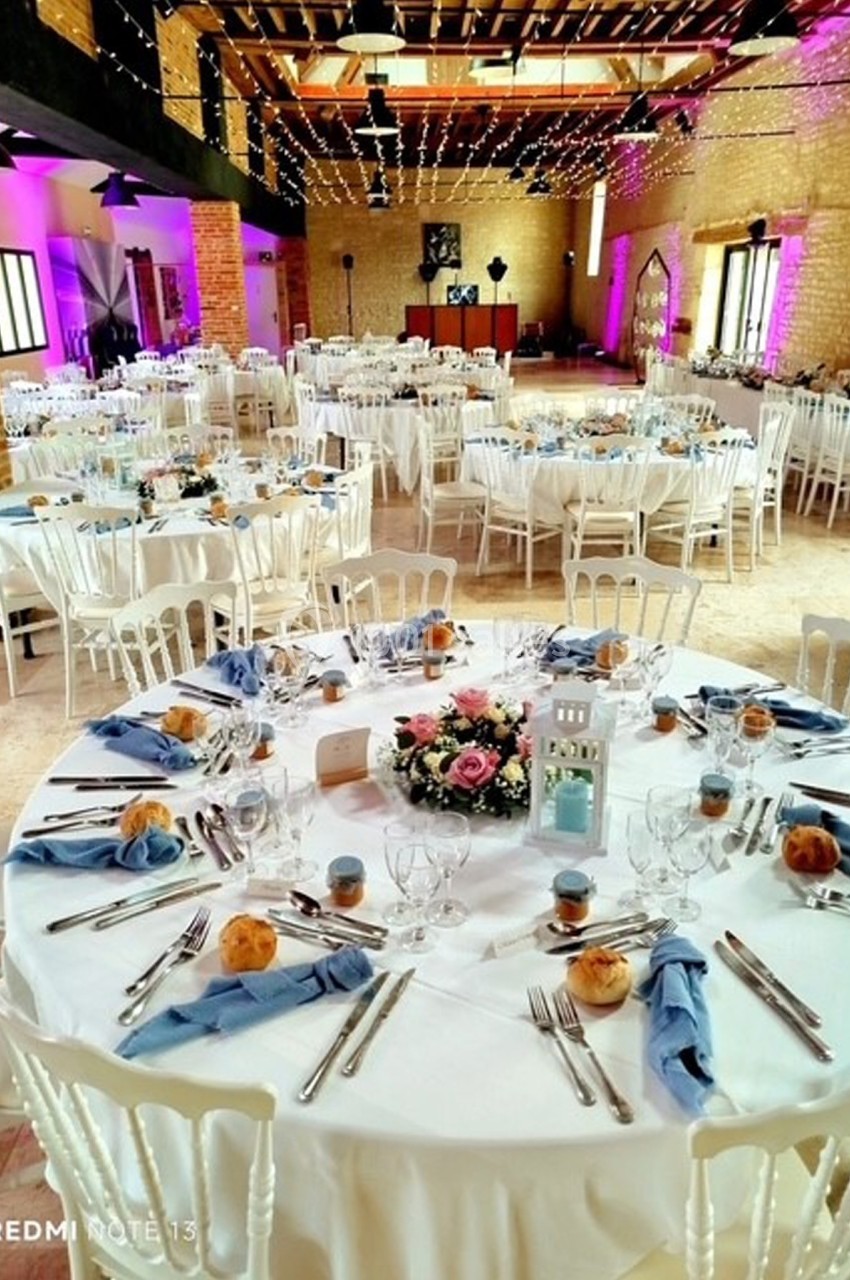 Salle de réception décorée avec des tables rondes dressées, nappes blanches, fleurs et éclairage chaleureux.