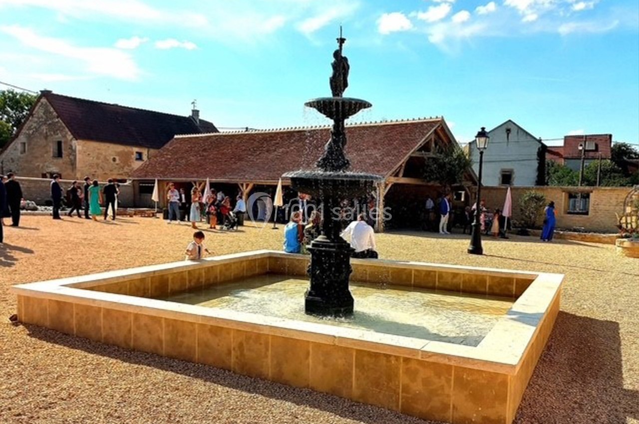 Fontaine en pierre noire au centre d'une cour pavée, entourée de bâtiments traditionnels et de visiteurs.