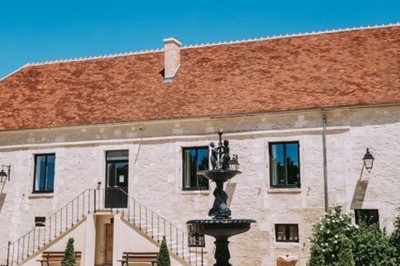 Table en bois avec un chapeau, un flacon de parfum, des sandales, un bouquet de fleurs et une bague devant un mur de briques.
