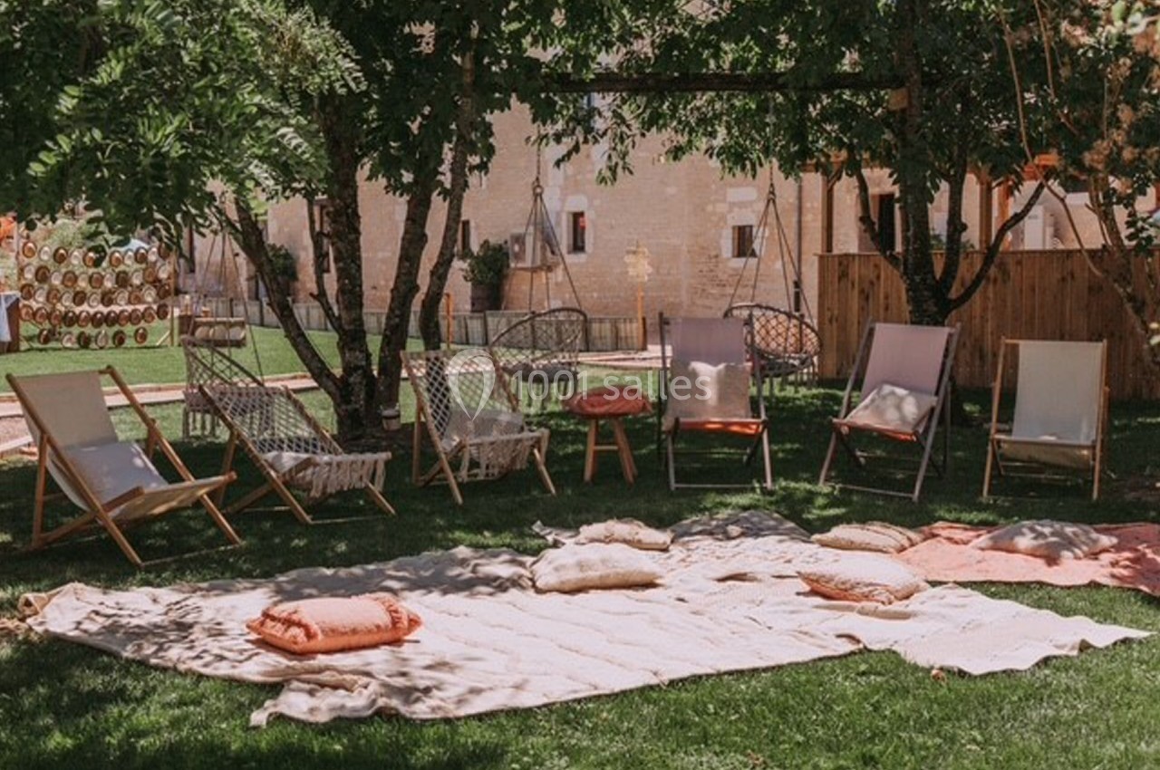 Chaises longues et coussins disposés sur une pelouse ombragée, entourés d'arbres et de décorations extérieures.