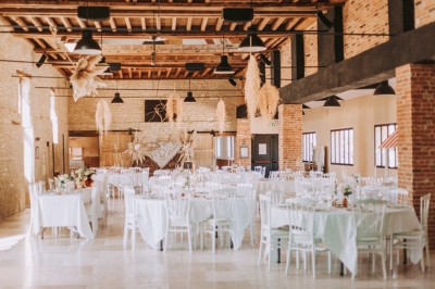 Table en bois avec un chapeau, un flacon de parfum, des sandales, un bouquet de fleurs et une bague devant un mur de briques.