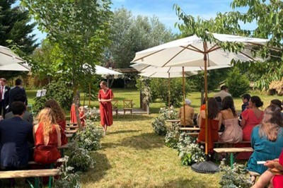 Table en bois avec un chapeau, un flacon de parfum, des sandales, un bouquet de fleurs et une bague devant un mur de briques.