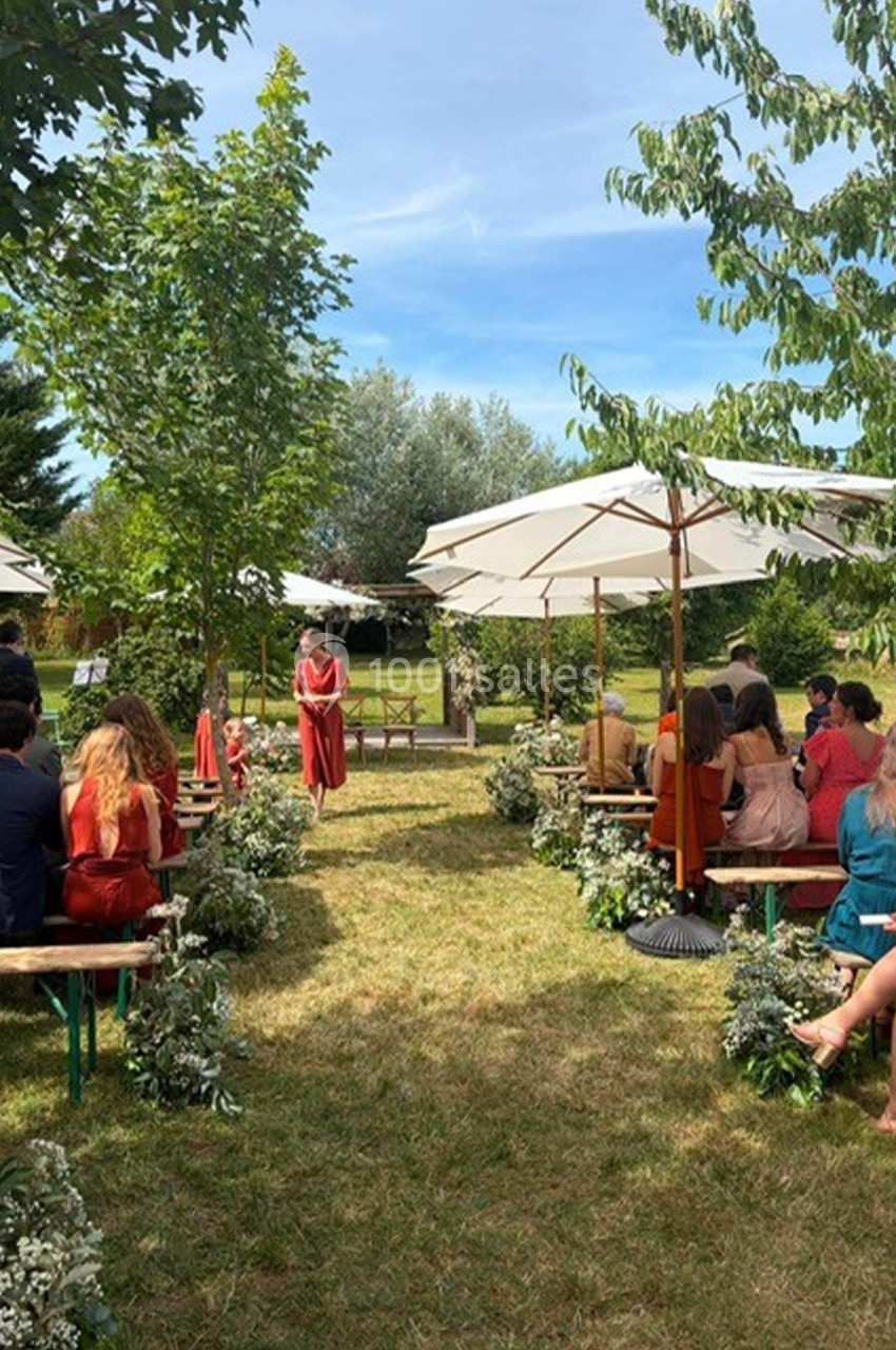 Invités assis sur des bancs en bois lors d'une cérémonie en plein air, entourés de verdure et de fleurs.