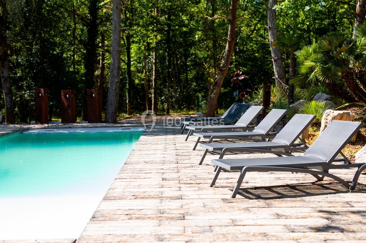 Chaises longues alignées au bord d'une piscine entourée de végétation et de pavés ensoleillés.