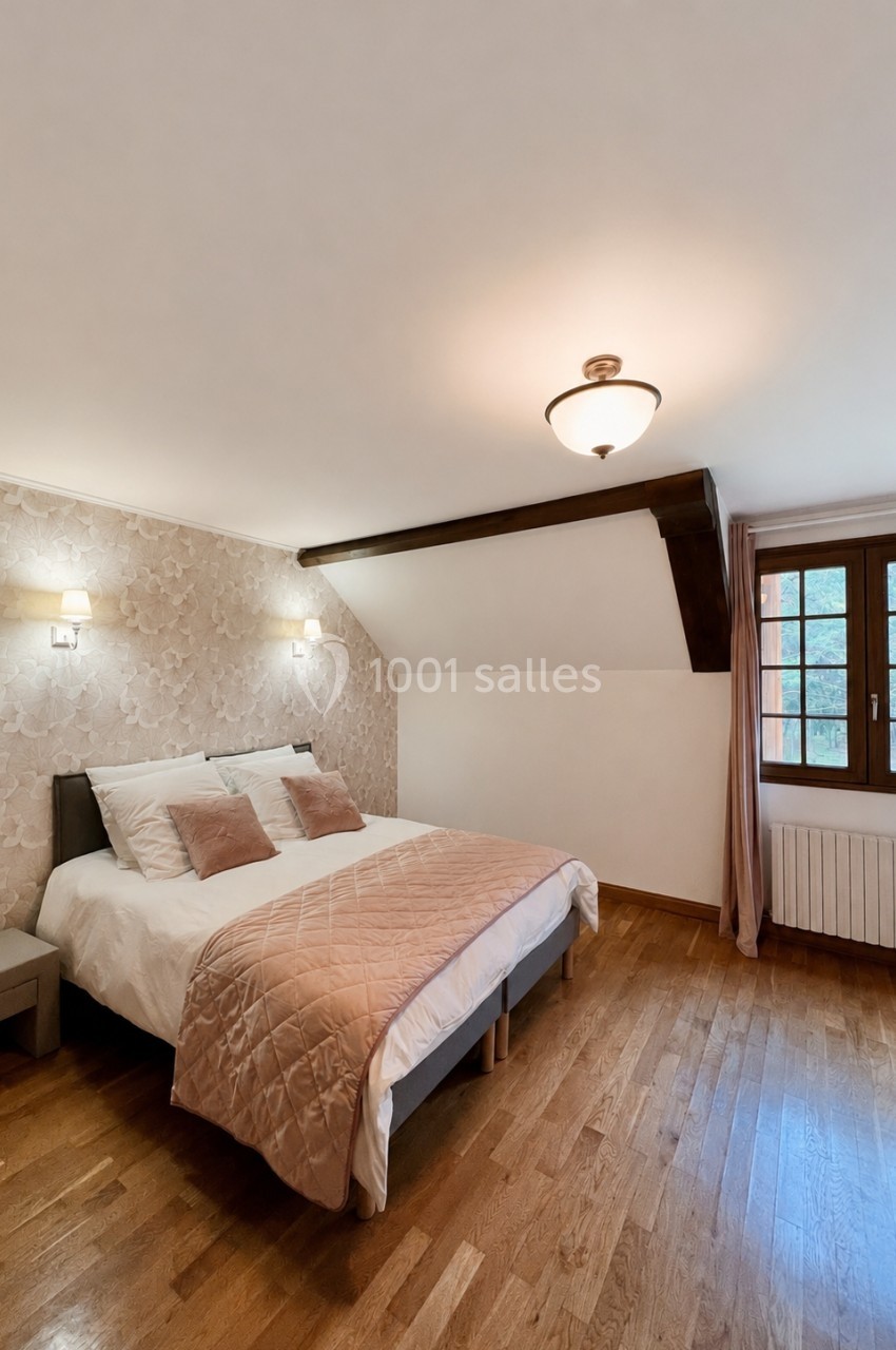 Chambre lumineuse avec lit double, parquet en bois, murs clairs, et fenêtre donnant sur l'extérieur.