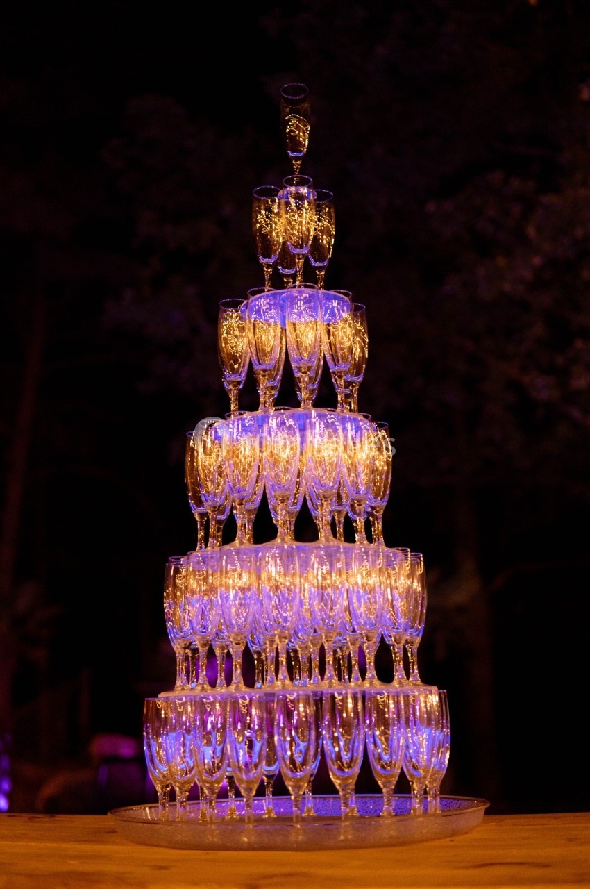 Tour de coupes à champagne empilées en pyramide, éclairées par une lumière violette dans un environnement sombre.