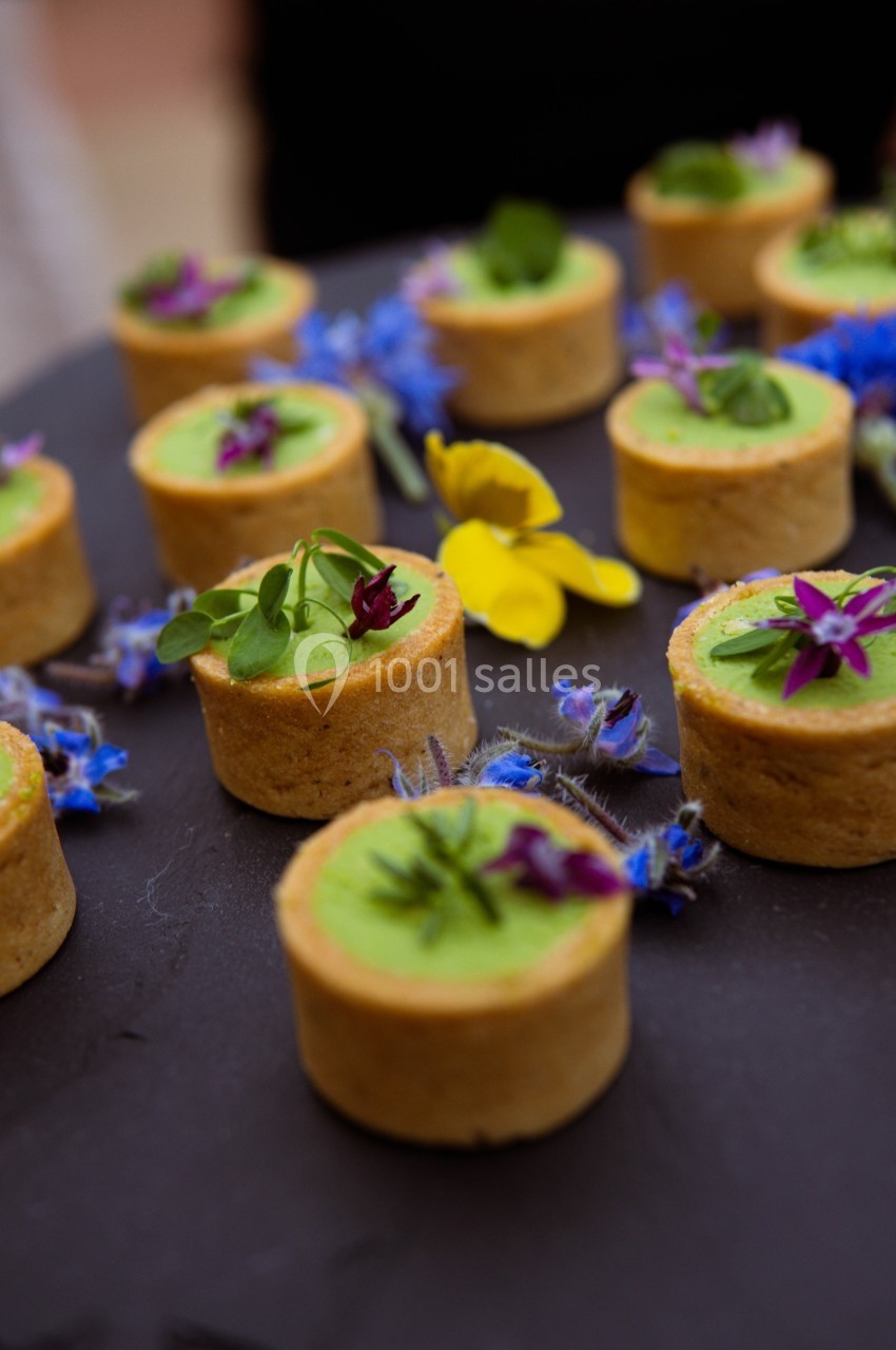 Tartelettes garnies de crème verte, décorées de fleurs comestibles colorées, présentées sur un plateau noir.