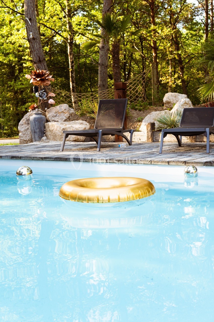 Bouée dorée flottant dans une piscine entourée de chaises longues et de végétation.