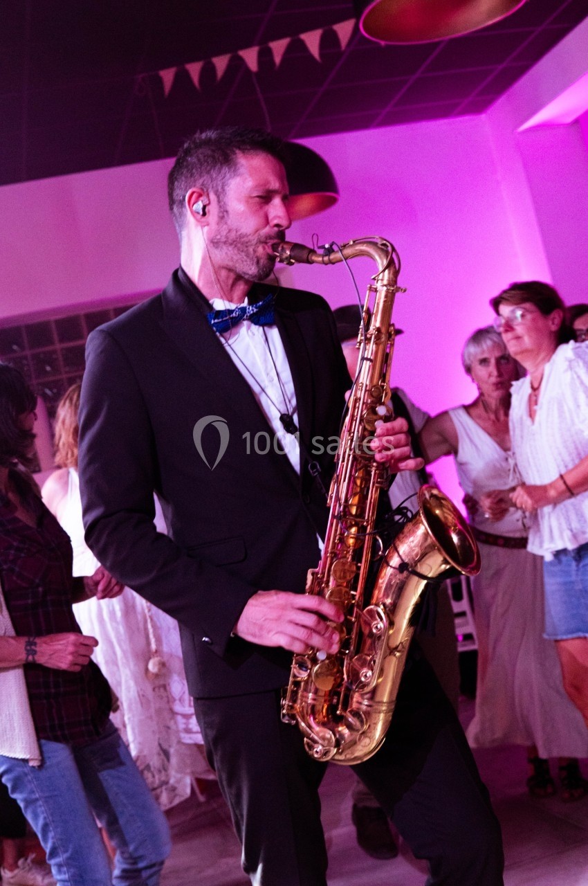 Un musicien en costume joue du saxophone lors d'un événement festif dans une salle éclairée de lumières roses.