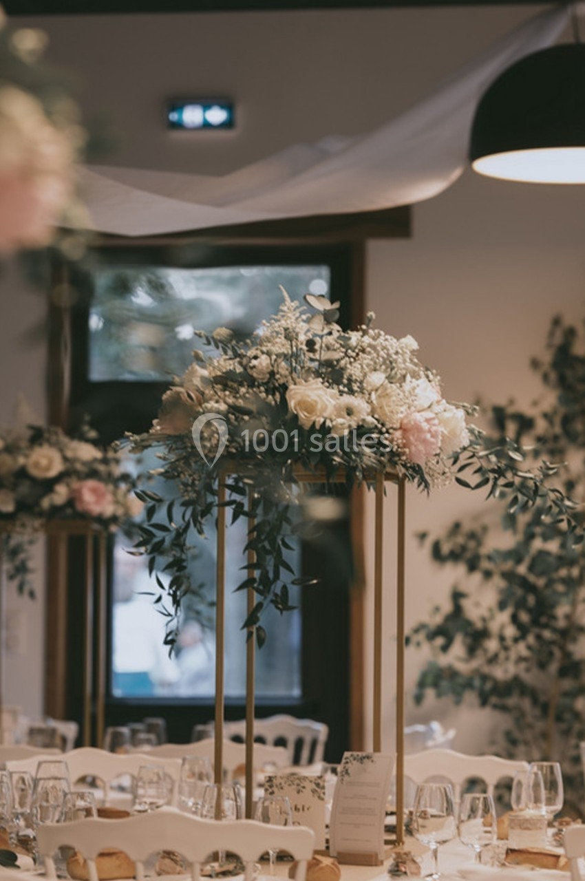 Centre de table floral avec roses et feuillage sur support doré, dans une salle de réception élégamment décorée.