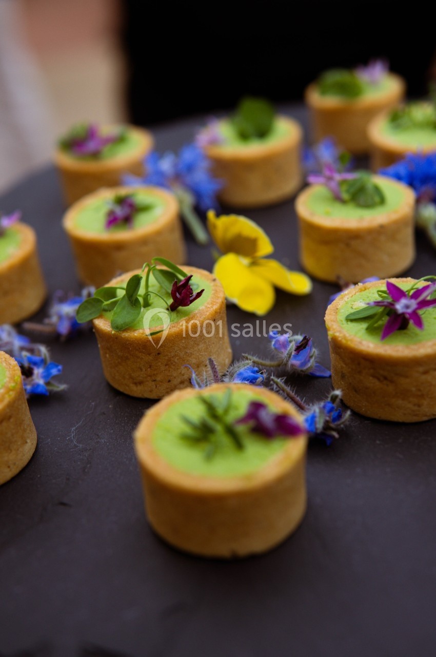 Tartelettes garnies de crème verte et décorées de fleurs comestibles colorées sur un plateau noir.