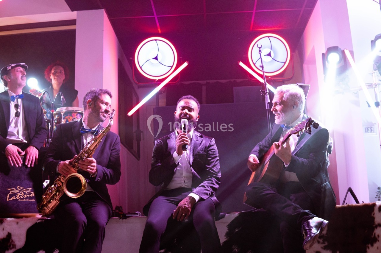 Un chanteur accompagné de musiciens jouant du saxophone et de la guitare sur une scène éclairée.