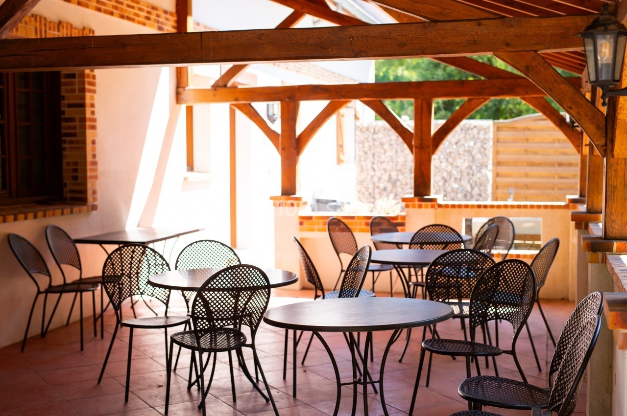 Terrasse couverte avec des tables rondes en métal noir et des chaises assorties, entourée de structures en bois.