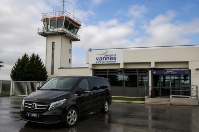 Miniature Vtc Hrc #5 Minibus noir stationné devant l'entrée de l'aéroport de Vannes avec une tour de contrôle en arrière-plan.